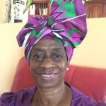 Woman in colorful headwrap, smiling indoors.